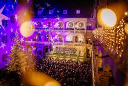 Feierlich beleuchteter Innenhof des Alten Schlosses mit Chorknaben, Weihnachtsbaum und Lichtreflexionen.