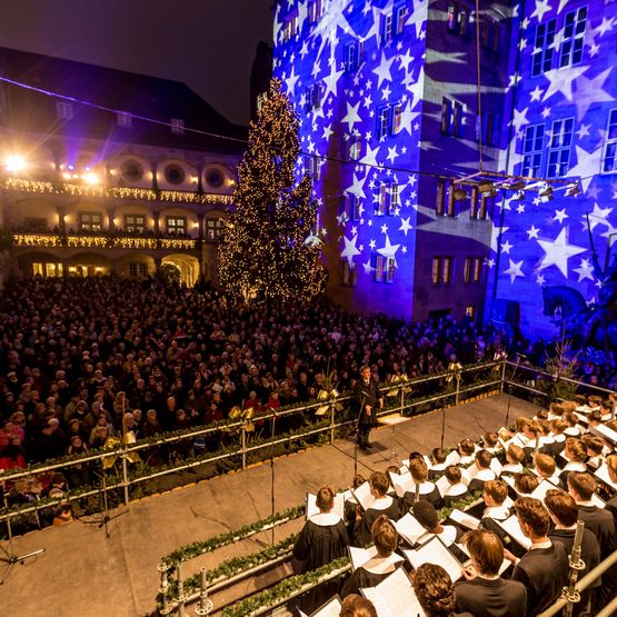 Stimmungsvolle Eröffnung des Weihnachtsmarktes im Innenhof des Alten Schlosses mit den Hymnus Chorknaben vor einer blau beleuchteten Wand mit weißen Sternen